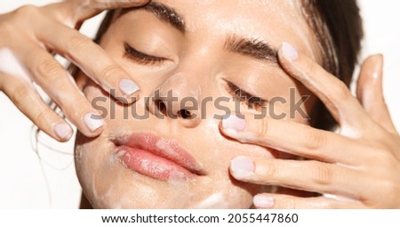 Close up portrait of beautiful woman clean her skin with cleansing gel, washing face and smiling from pleasure, standing over white background