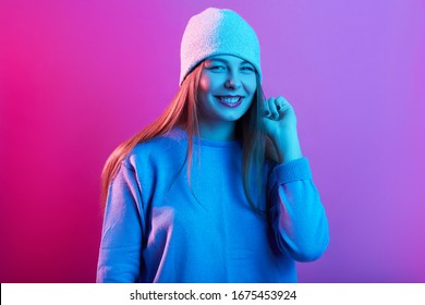 Close Up Portrait Of Beautiful Woman Dresses Casual Sweater And Cap, Young Lady With Toothy Smile Looking Directly At Camera, Posing Isolated On Pink Neon Background, Girl With Happy Facial Expression