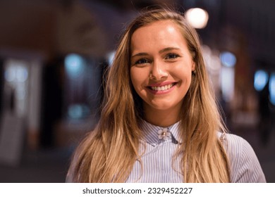 Close up portrait of a beautiful woman with long blonde hair outdoors in the city center in the evening.