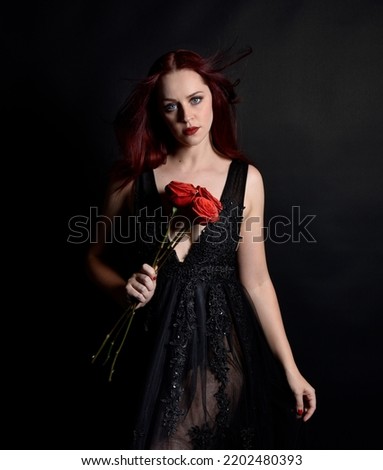 close up portrait of beautiful woman with red hair, wearing black dress with  elegant gestural hand poses on a dark studio background with moody lighting.