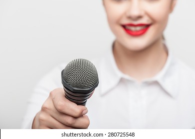 Close Up Portrait Of Beautiful Woman Tv Reporter With Caucasian Appearance And Bright Red Lips, Who Is Smiling And Proposes Someone To Give Her The Interview Holding The Microphone.