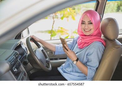 close up portrait of beautiful woman wearing hijab holding a smartphone while driving a car