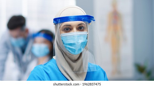 Close Up Portrait Of Beautiful Young Arabic Female Healthcare Specialist Wearing Medical Mask And Face Shield Protection In Hospital Looking At Camera Woman Nurse Or Doctor During Coronavirus Pandemic