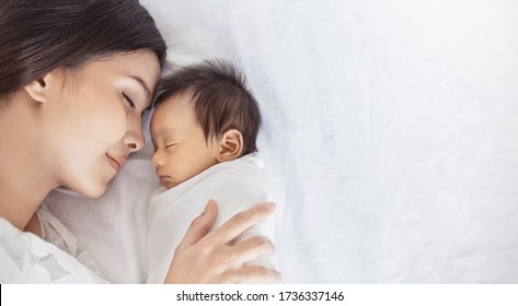 Das Porträt eines wunderschönen jungen asiatischen oder kaukasischen Muttermädchens, das ihr gesundes Neugeborenes küsst, schlafen im Bett mit Kopierraum. Gesundheitsfürsorge und medizinische Liebe Asia Lifestyle Mutter Tageskonzept