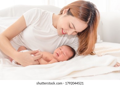 Close Up Portrait Of Beautiful Young Asian Mother With Newborn Baby. Side View Of A Young Woman Playing With Her Little Baby In Bed.