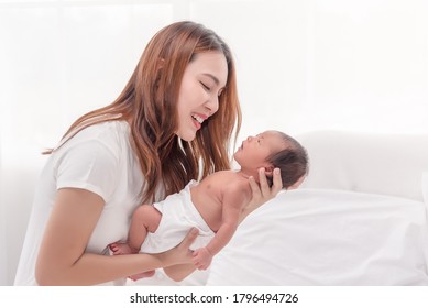 Close Up Portrait Of Beautiful Young Asian Mother With Newborn Baby. Side View Of A Young Woman Playing With Her Little Baby In Bed.