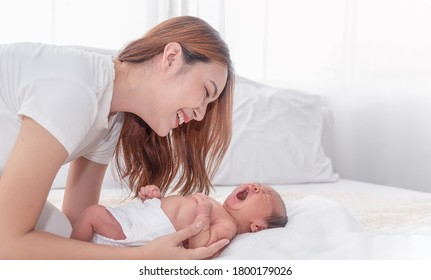 Close Up Portrait Of Beautiful Young Asian Mother With Newborn Baby. Side View Of A Young Woman Playing With Her Little Baby In Bed.