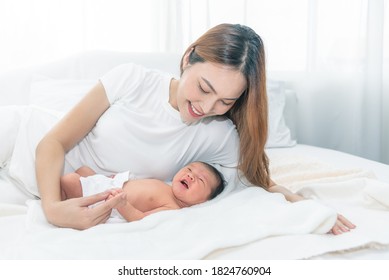 Close Up Portrait Of Beautiful Young Asian Mother With Newborn Baby. Side View Of A Young Woman Playing With Her Little Baby In Bed.