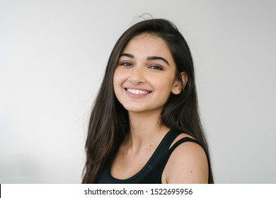 Close up portrait of a beautiful, young attractive and elegant Indian Asian woman against a white background. She is in exercise attire and is smiling confidently. 

