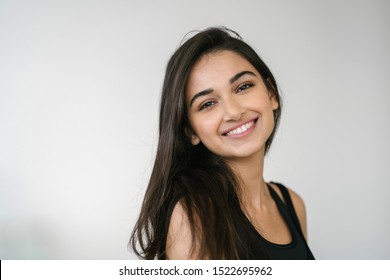 Close up portrait of a beautiful, young attractive and elegant Indian Asian woman against a white background. She is in exercise attire and is smiling confidently. 
