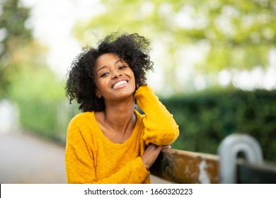 Close Up Portrait Of Beautiful Young Black Woman Relaxing On Bench Outside And Smiling