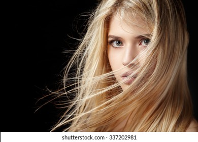Close portrait of a beautiful young blonde woman with flying hair on a black background.