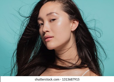 Close Up Portrait Of Beautiful Young Woman With Perfect And Clean Skin. Korean Female Model With Hairs Flying Looking At Camera Against Blue Background.