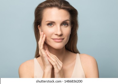 Close Up Portrait Of Beautiful Young Woman Isolated On Blue Studio Background Touch Clean Healthy Skin, Pretty Millennial Female Model Look At Camera Satisfied With Moisturized Hydrated Face Treatment