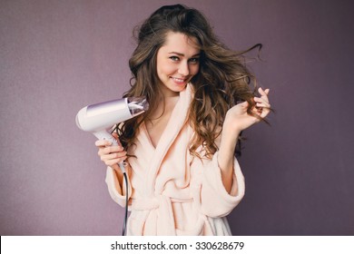  Close up portrait of beautiful young woman in pink bathrobe  drying hairstyle. Cute young  lady smiling .
