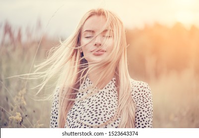 Close Up Portrait Of Beauty Girl With Fluttering White Hair Enjoying Nature Outdoors, On A Field. Flying Blonde Hair On The Wind. Breeze Playing With Girl's Hair. Beautiful Young Woman Face Closeup.