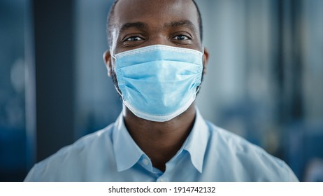 Close Up Portrait Of A Black African American Handsome Male In White Shirt Wearing A Protective Face Mask. Successful Man Calmly Looking At Camera. Stylish Businessman Or A Doctor In Hospital.