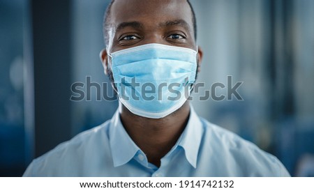 Close Up Portrait of a Black African American Handsome Male in White Shirt Wearing a Protective Face Mask. Successful Man Calmly Looking at Camera. Stylish Businessman or a Doctor in Hospital.