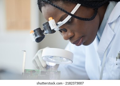 Close Up Portrait Of Black Female Engineer Inspecting Computer Parts With Magnifier At Quality Control Line