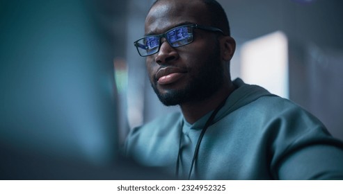 Close Up Portrait of Black Man Working on Computer, Lines of Code Language Reflecting on his Glasses. Male Programmer Developing New Software, Managing Cybersecurity Defence Project. - Powered by Shutterstock