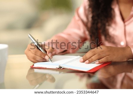 Close up portrait of a black woman hands writing in agenda on a desk