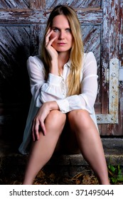 Close Up Portrait Of A Blond Woman With Blue Eyes Sitting In Front Of A Weathered Old Door