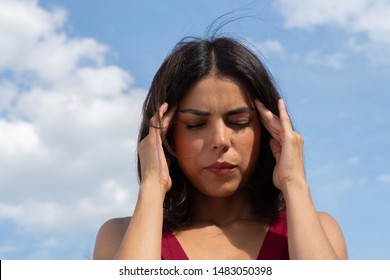 Close up portrait of a brunette woman rubbing her temples to alleviate an awful headache. Outdoors - Shutterstock ID 1483050398