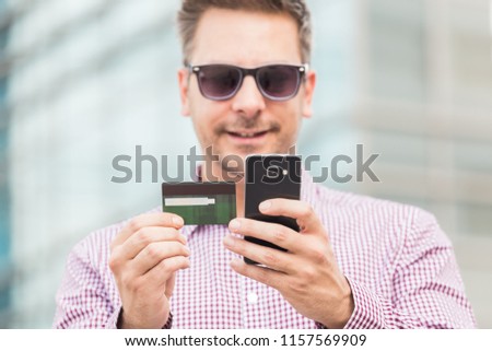 Close up portrait of businessman paying online with his credit card on office building background.
