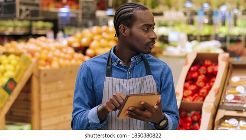 Close Up Portrait Of Busy African American Male Worker Standing In Supermarket And Typing On Tablet While Doing Inventory. Young Man Food Store Assistant At Work Tapping On Device. Retail Concept