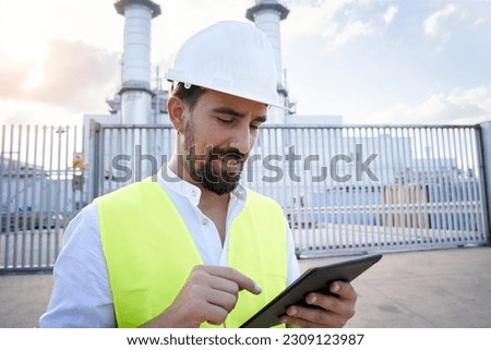 Close up portrait of a caucasian engineer using digital tablet to do an inspection at thermoelectric plant. Worker outside power station introducing data to an electronic device. High quality photo