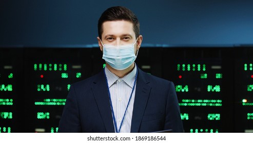 Close up portrait of Caucasian man system administrator in mask standing in High Tech big data center checking security of processors working with digital information and typing on tablet Work concept