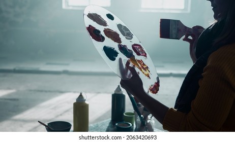 Close Up Portrait Of A Caucasian Young Artist Holding A Palette Filled With Colours, Background Is An Old Empty Warehouse With Big Windows. Painter Tools.