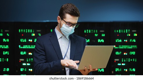 Close up portrait of Caucasian young man wearing mask standing among servers and typing on laptop, checking big data processors. Male analytic in big data storage working on digital security - Powered by Shutterstock - Get 15% off with code: PIKWIZARD15