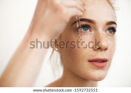 Close up portrait of a charming red haired woman with freckles applying hyaluronic serum on her face isolated on white. 商業照片 © 