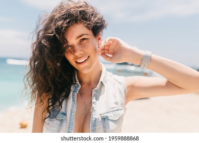 Close Up Portrait Of Charming Smiling Woman With Wavy Hair Looking At Camera And Holding Hand Near Face On Background Of Ocean. High Quality Photo