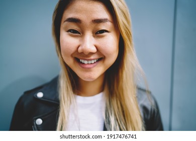 Close up portrait of cheerful Asian hipster girl with perfect white teeth smiling at camera, happy Chinese female 20 years old posing at urban setting enjoying pastime leisure and youth lifestyle