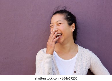 Close Up Portrait Of Cheerful Asian Woman Laughing With Hand On Mouth Against Purple Wall