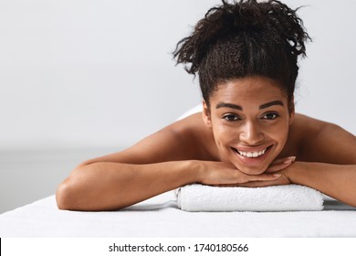 Close up portrait of cheerful pretty black girl lying on massage table, empty space