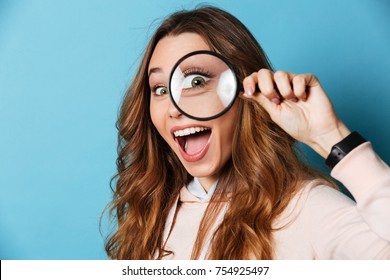 Close up portrait of a cheerful pretty girl looking through magnifying glass isolated over blue background - Powered by Shutterstock