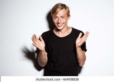 Close up portrait of cheerful smiling blond handsome young man wearing black t-shirt clapping hands isolated on white background