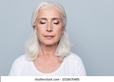 Close up portrait of confident concentrated mature woman with wrinkles on face, with closed eyes, with nude make up, isolated on gray background