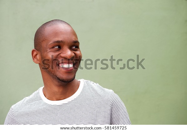 Close up portrait of\
confident young black man looking sideways and smiling against\
green background