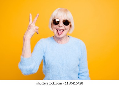 Close Up Portrait Of Crazy Modern Grandma Stuck Out Her Tongue And Showing V-sign Isolated On Yellow Background