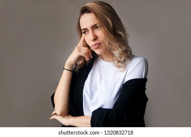 Close up portrait of curly blonde confident thoughtful girl, holding hand near the face, looking seriously up, standing over grey background with copy space