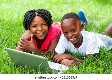 Close Up Portrait Of Cute African Kids Laying On Grass With Laptop.