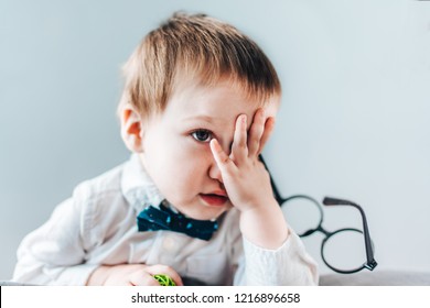 Close Up Portrait Of Cute Baby Boy Wearing Smart Outfit Hiding His Face With A Palm Looking Very Dissapointed. Plain Gray Background.