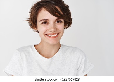 Close up portrait of cute girl with short hairstyle and clean smooth skin, smiling happy at camera, standing against white background. - Shutterstock ID 1927519829