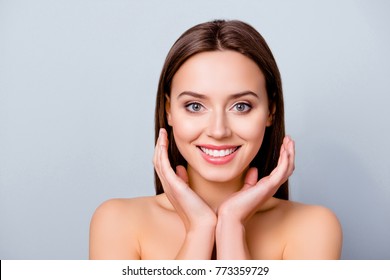 Close up portrait of cute joyful pretty young woman with excellent skin and beaming smile, she is admiring her beauty in a mirror, isolated on grey background, copyspace