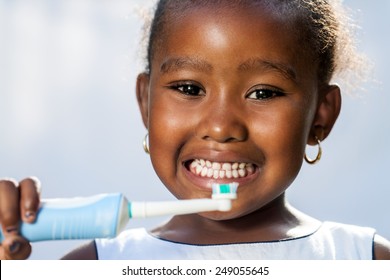Close up portrait of cute little Afro girl holding electric toothbrush ready to brush teeth.