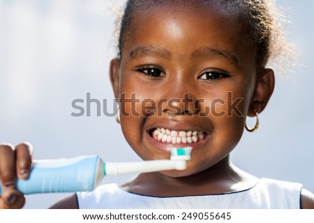 Close up portrait of cute little Afro girl holding electric toothbrush ready to brush teeth.